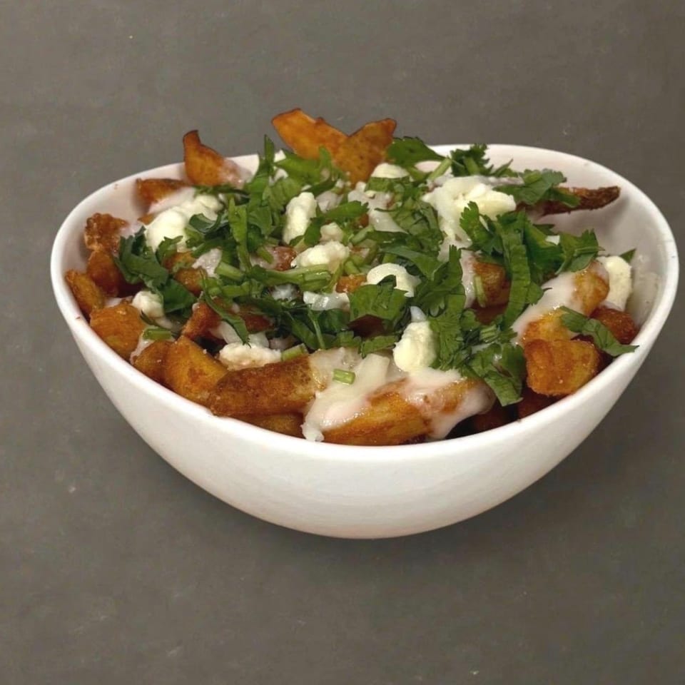 A white bowl filled with golden-brown tater tots, melted cheese, and fresh green herbs.