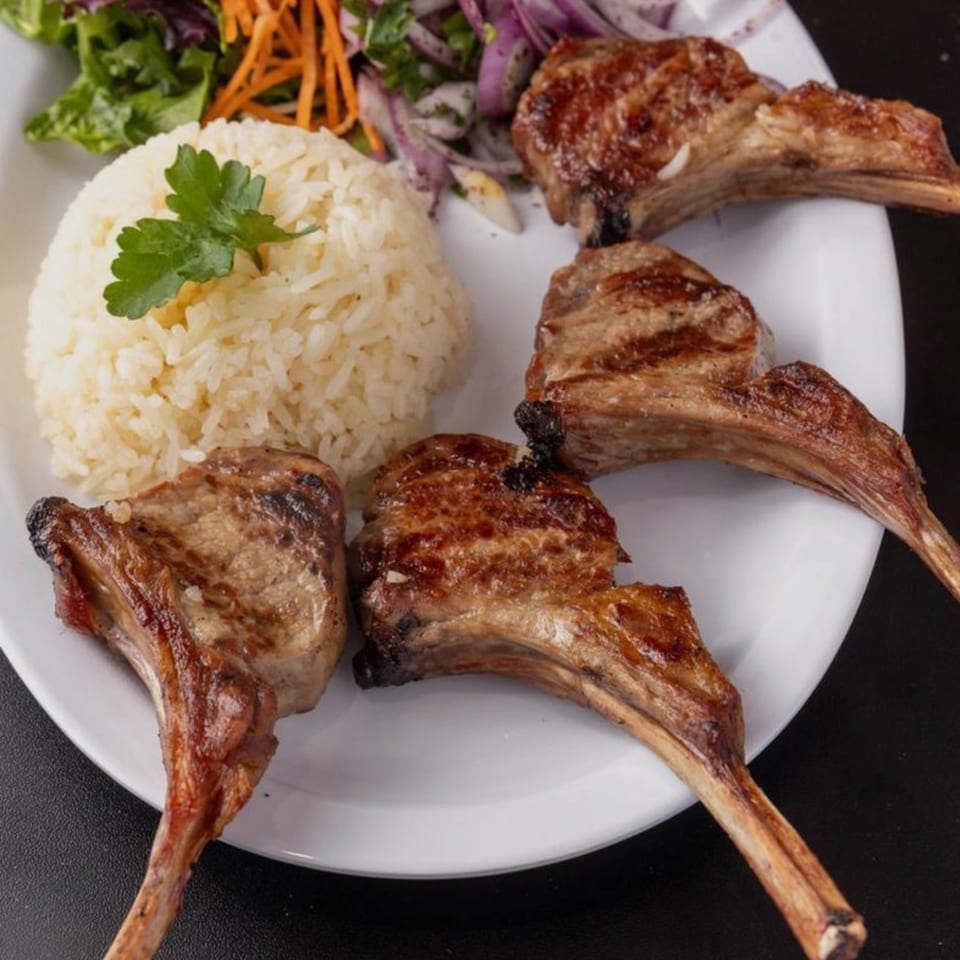 Four grilled lamb chops with rice, a sprig of parsley, and a side salad.